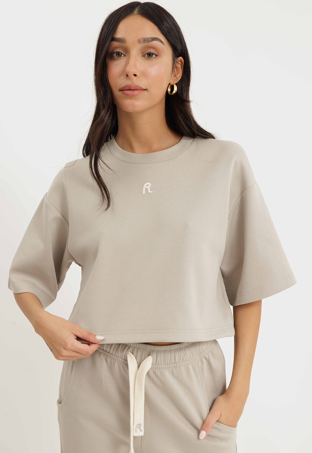 טי-שירט קרופ לנשים בצבע אבן עם לוגו קטן בחזה ושרוולים רחבים בגזרת אוברסייז.