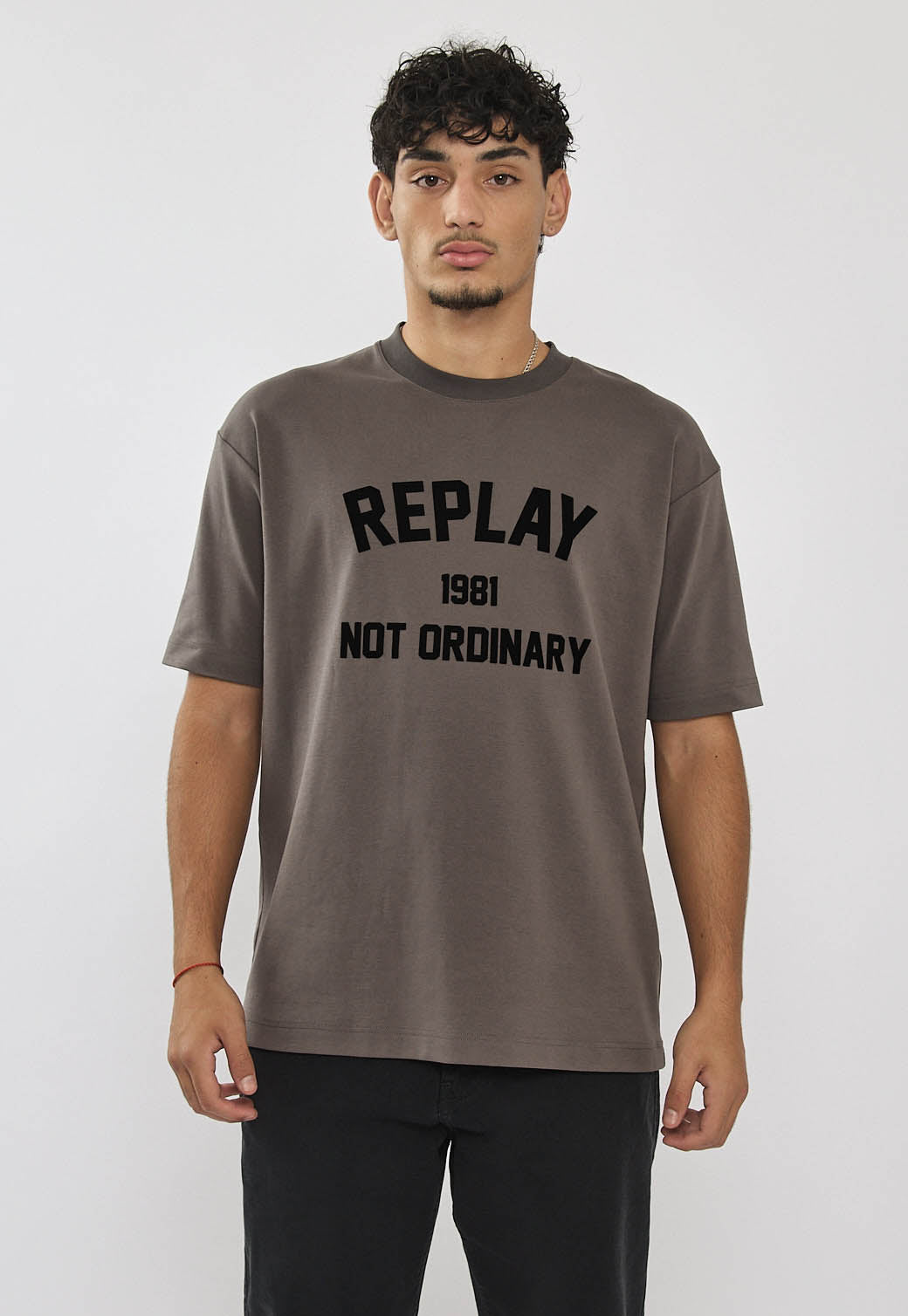 גבר לובש טי-שירט אוברסייז אפורה עם הדפס לוגו גדול בחזית.