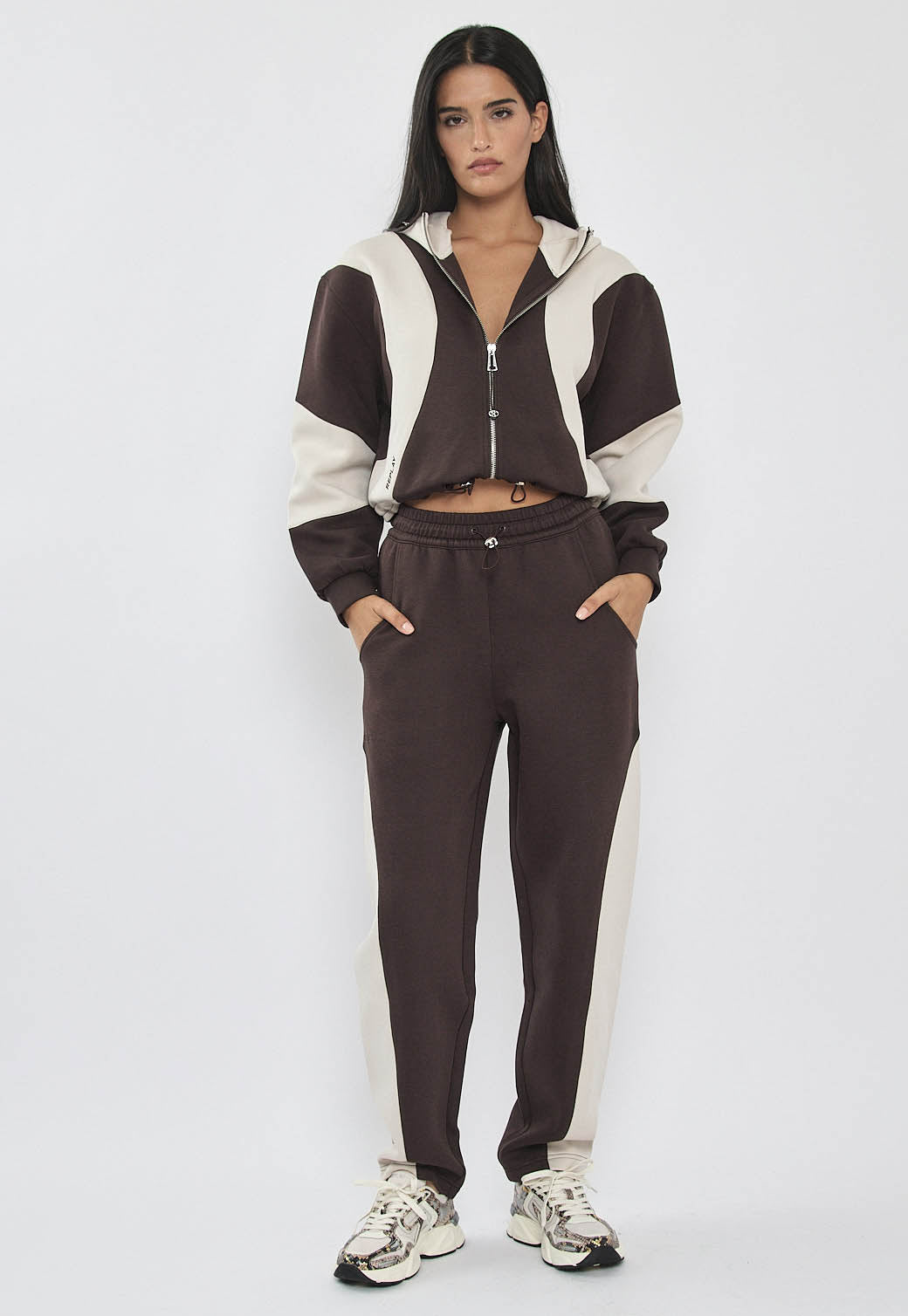 מכנסי ג’וגר לנשים בצבע קרם עם פאנלים צדדיים כהים, מותן אלסטית ושרוך, ושולי ריבס בקרסוליים.